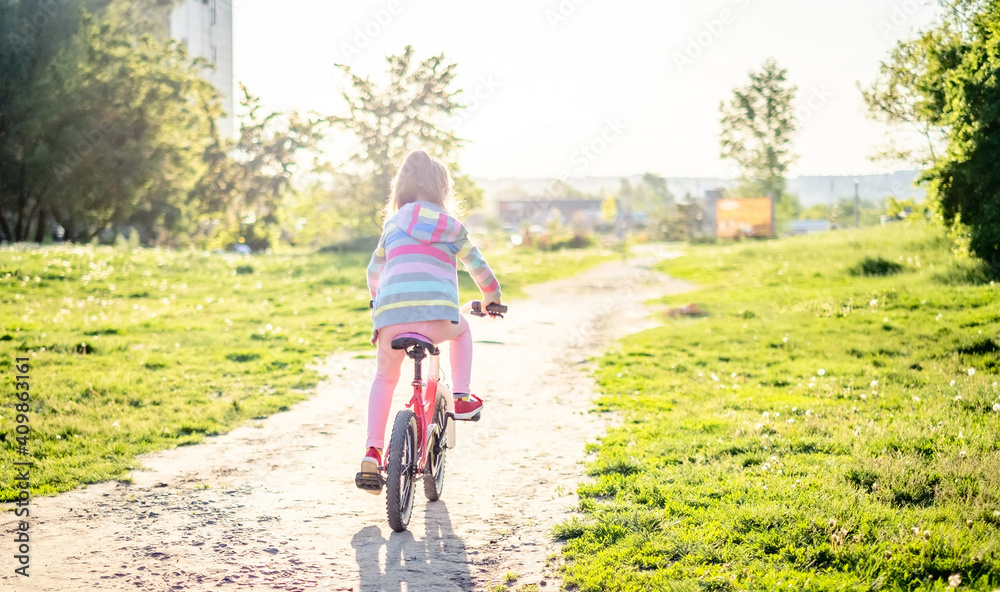 Cyclist preteen girl riding on bike through green sunny park, from the back Cyclist preteen girl riding on bike through green sunny park, from the back