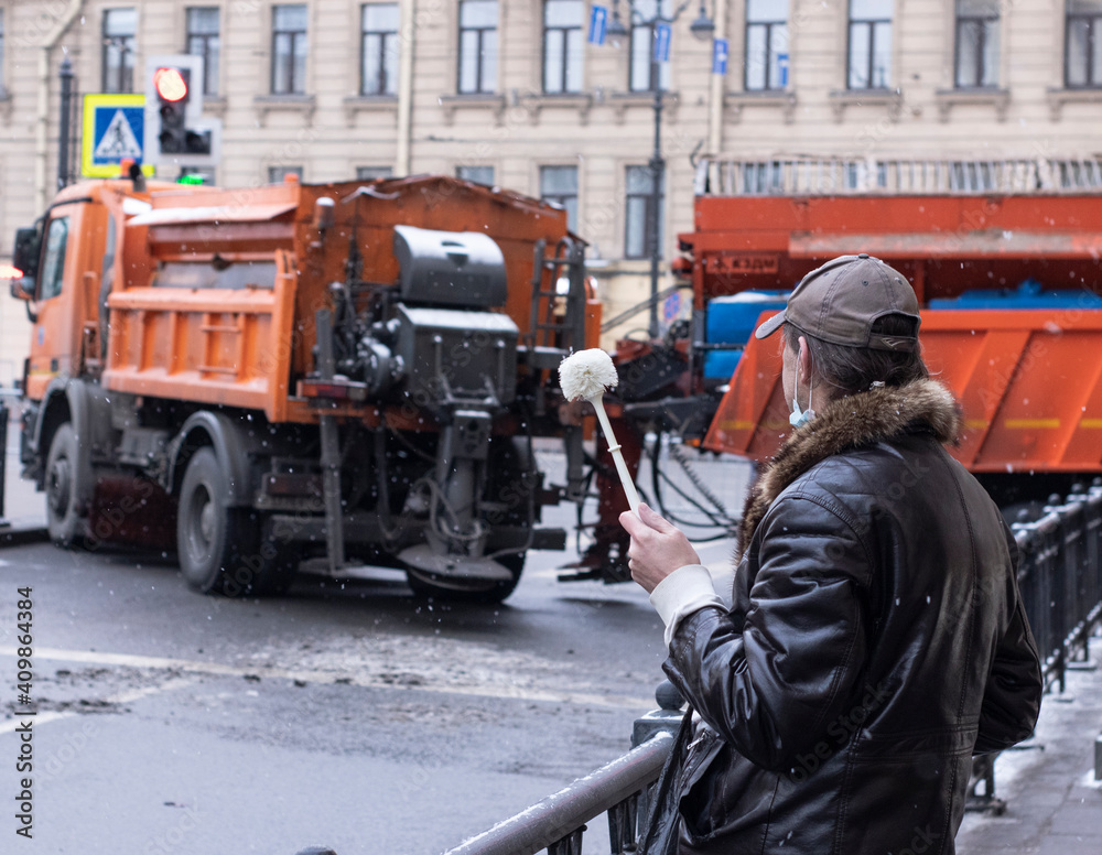 Fototapeta premium a man in warm clothes with a toilet brush in his hand stands on a partitioned city street. Rally in St. Petersburg, Russia, January 31, 2021 man with a brush in the city center