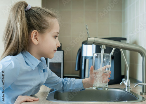 Child is holding a transparent glass. Filling cup beverage. Pouring fresh drink. Consumption of tap water contributes to the saving of water in plastic bottles and to the protection of the environment