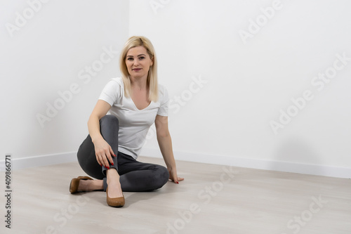 Young blonde smiling woman sitting cross-legged over white wall