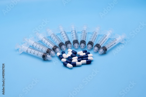 multiple clear plastic 5ml syringes with blue and white capsule tablets isolated against a blue background