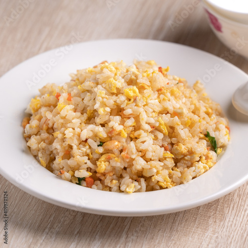 Chinese fried rice in white plate on bright wooden table background.