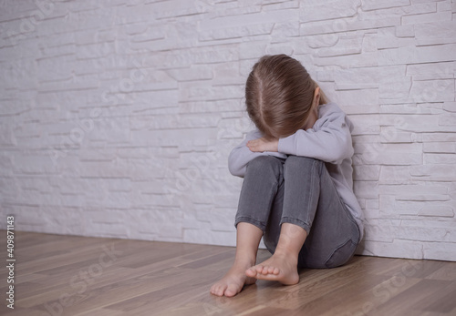 Upset little child girl crying covering face with hands sitting alone on floor, sad lonely orphan kid being bullied abused feeling stressed or scared, children violence abuse concept