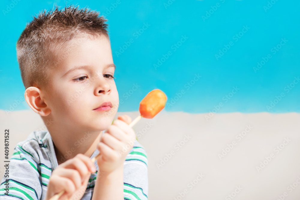 Beautiful child eats fresh carrot on a stick. Boy gnaws vegetables on a blue background. Beautiful child eats fresh carrot on a stick. Boy gnaws vegetables on a blue background.
