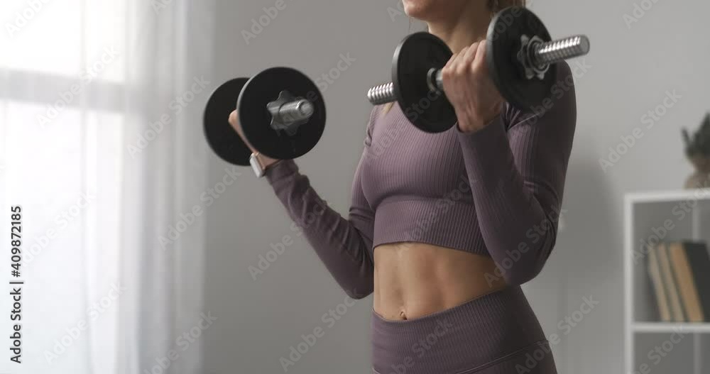 slender sportswoman is training with dumbbells at home,details of sporty body, fitness and healthy lifestyle