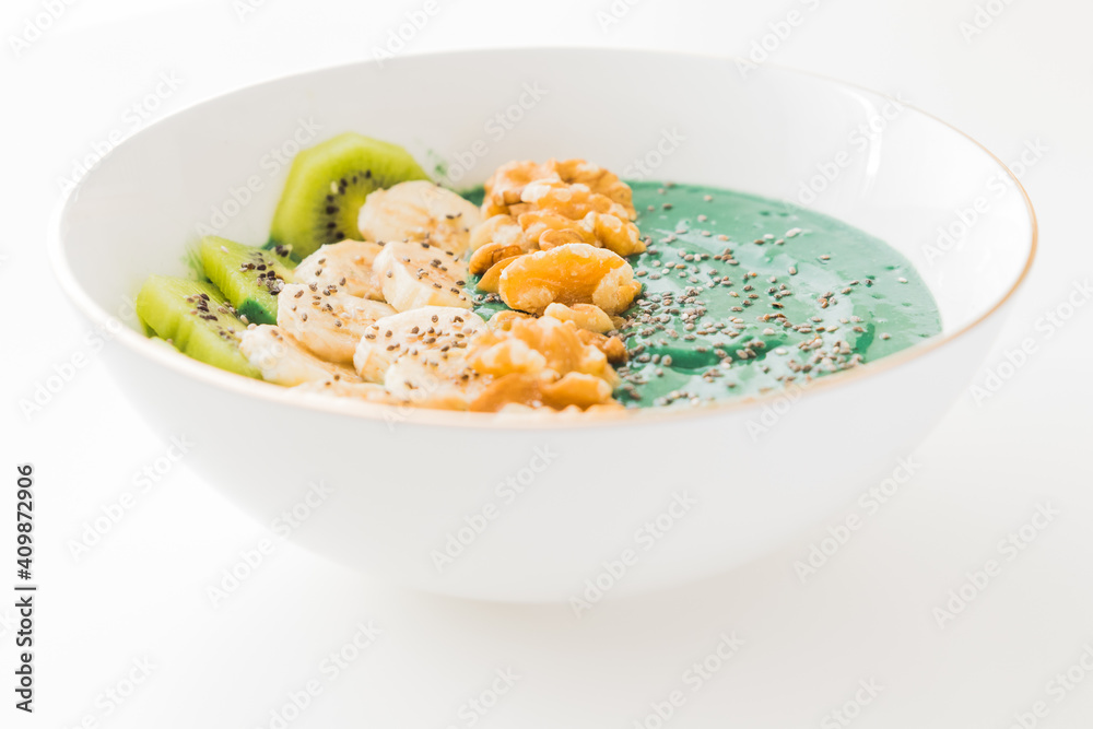 spirulina smoothie bowl with banana, walnuts, kiwi and chia seeds on white background