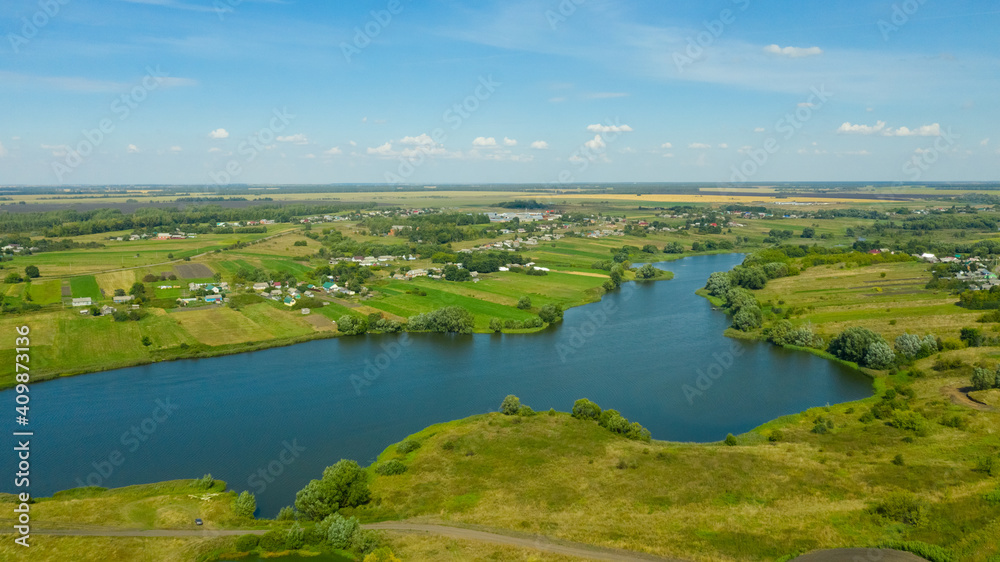 Aerial view of the river surrounded by green fields through which the river flows. Rural landscape in the countryside.
