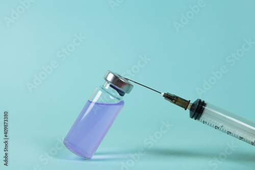Covid-19 Recorded vaccine bottle with liquid and extracting vaccine from it with a syringe on a blue background