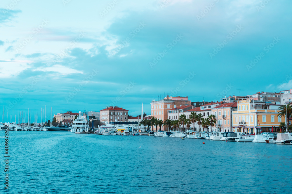 View of Zadar city embankment with residential buildings, palm trees and moored boats, Croatia