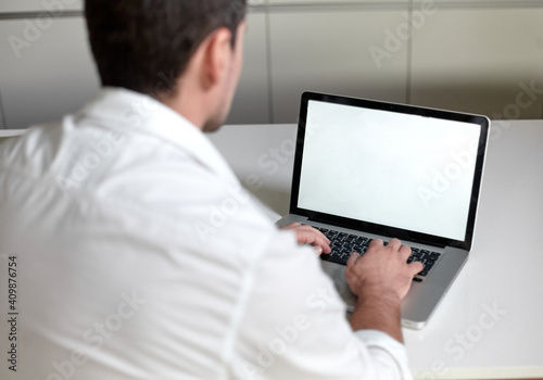 Frame view of man in casual clothes using a laptop while sitting at the table in office.