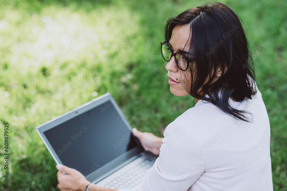 Young woman using laptop with blank screen in public park while working outdoors. Distance learning and teleworking during a pandemic. Soft selective focus. Young woman using laptop with blank screen in public park while working outdoors. Distance learning and teleworking during a pandemic. Soft selective focus.