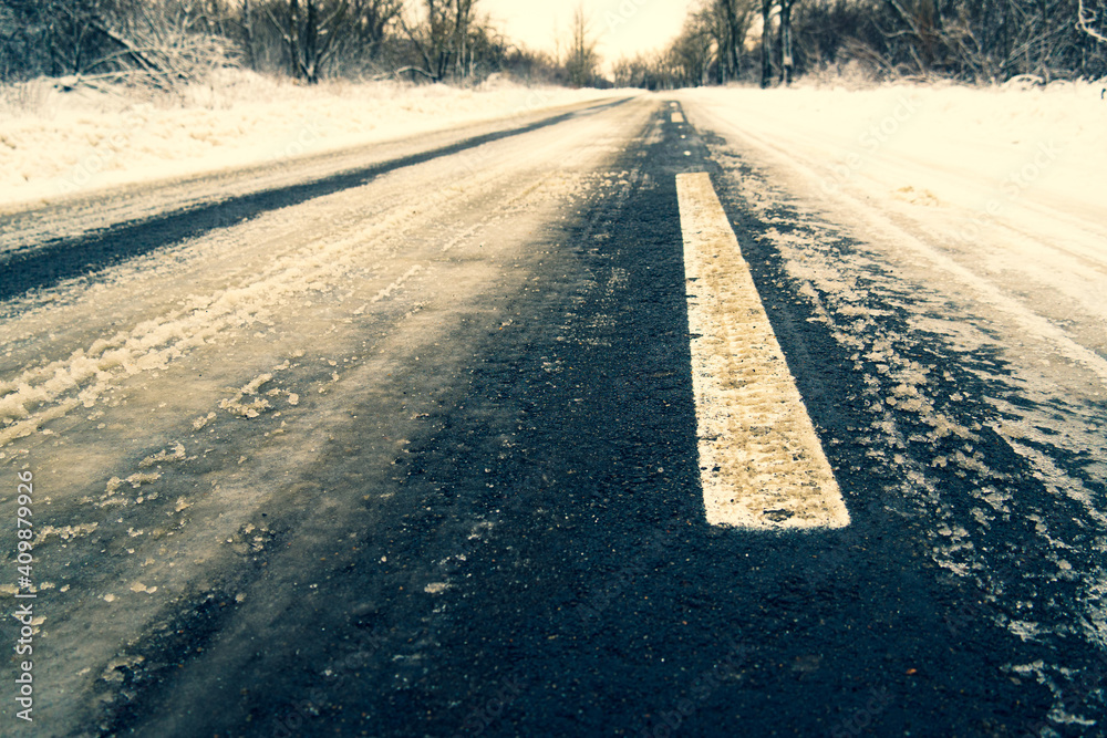 The road under the dirty melting snow in winter, Dividing lines are visible on the roadway The road under the dirty melting snow in winter, Dividing lines are visible on the roadway