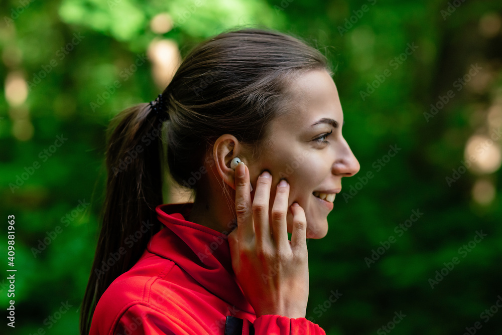 girl straightens a wireless earpiece in the park before jogging girl straightens a wireless earpiece in the park before jogging