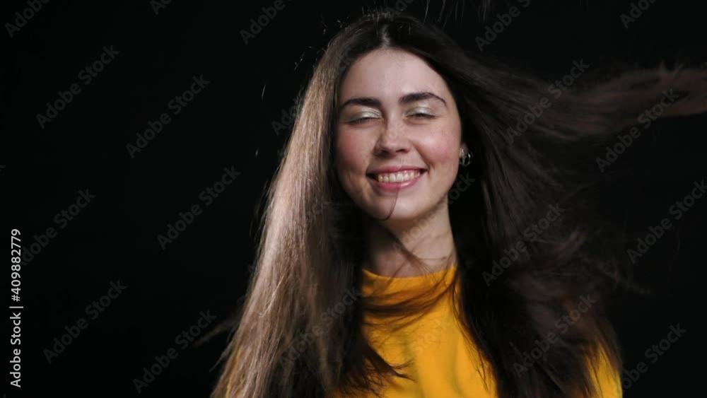 Portrait of a young smiling woman posing on a black background, and her hair from below blows the air. Slow motion. Portrait of a young smiling woman posing on a black background, and her hair from below blows the air. Slow motion.