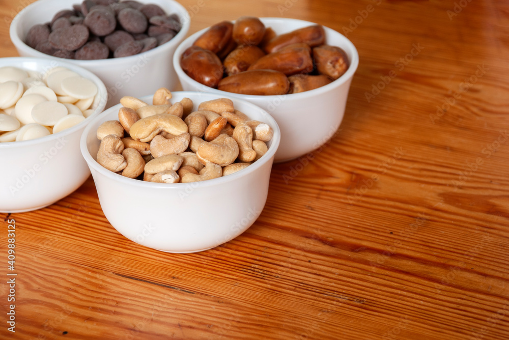 Food ingredients in white bowls. Cashews, dates, white and milk chocolate drops in white small bowls. Food ingredients in white bowls. Cashews, dates, white and milk chocolate drops in white small bowls.