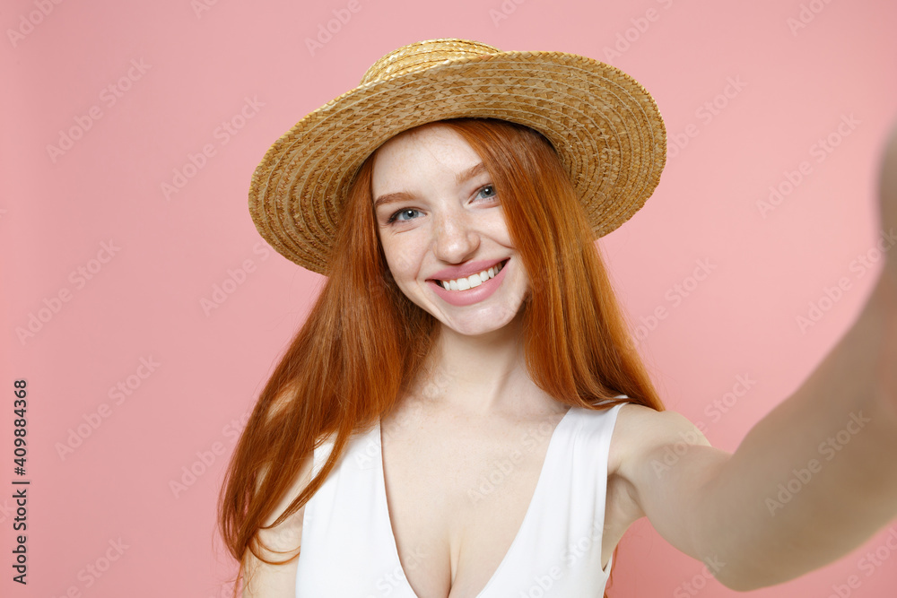 Young smiling caucasian cheerful nice redhead woman 20s ginger long hair wearing straw hat summer clothes doing selfie shot on mobile phone isolated on pastel pink color background studio portrait. Young smiling caucasian cheerful nice redhead woman 20s ginger long hair wearing straw hat summer clothes doing selfie shot on mobile phone isolated on pastel pink color background studio portrait.