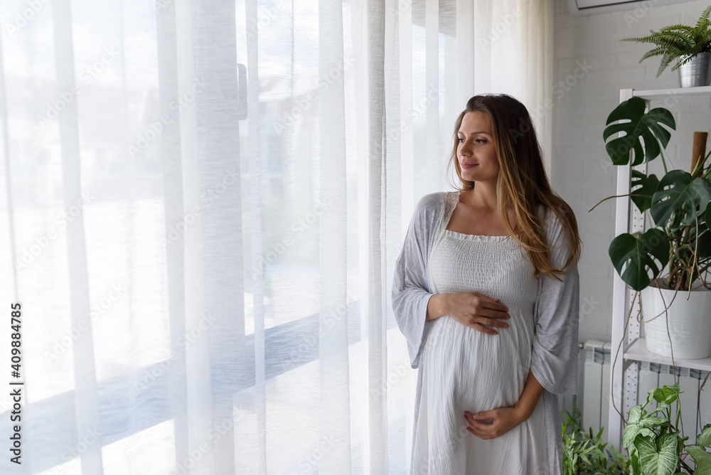 Portrait of a beautiful smiling pregnant woman looking through the window Portrait of a beautiful smiling pregnant woman looking through the window