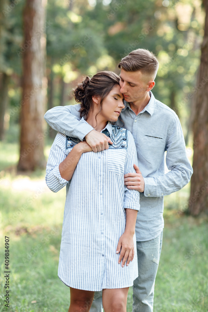 Fototapeta premium Cheerful young woman and man are hugging outdoors in summer park. Dating and romantic vacation. couple in love gently looking at each other on sunny day. Love and relationships between young people