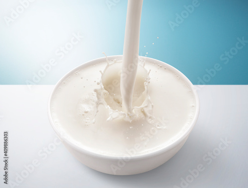 Fresh milk pouring in bowl with splash. isolated on blue and white background.