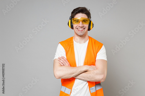 Photography Young employee happy handyman man in orange vest protective ear muffs look camera hold hands crossed folded isolated on grey background studio Instruments for renovation apartment Repair home concept