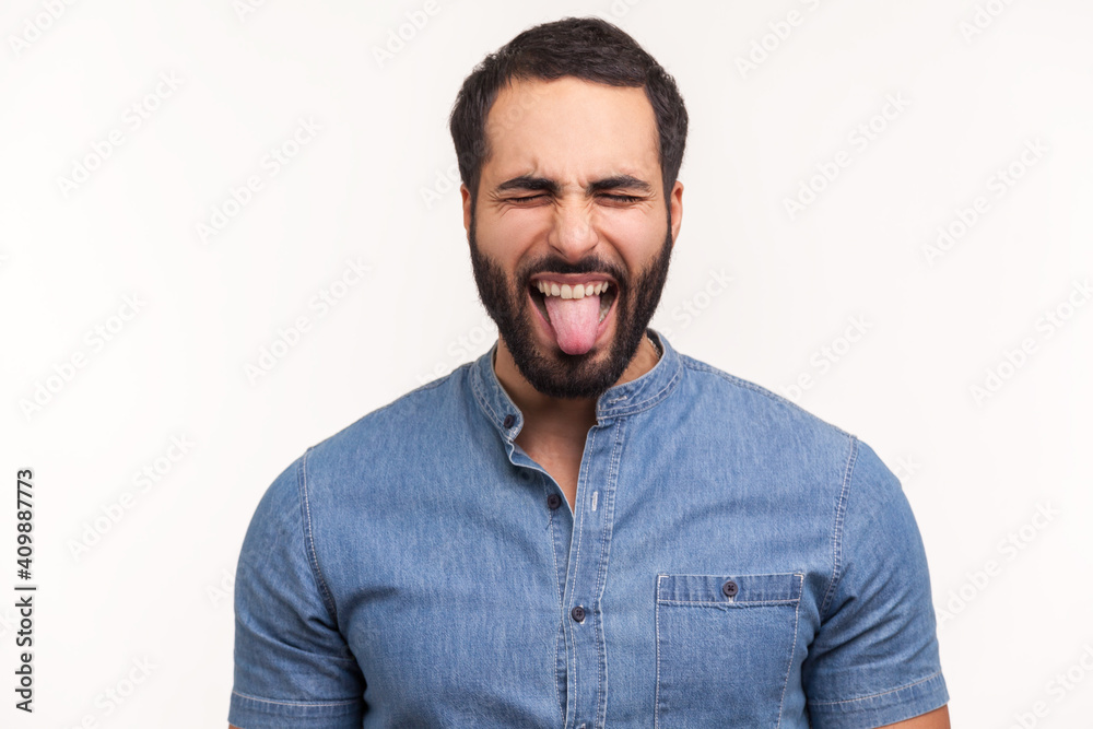 Naughty infantile man with beard closing eyes and showing tongue, having fun, fooling around, childish manners. Indoor studio shot isolated on white background Naughty infantile man with beard closing eyes and showing tongue, having fun, fooling around, childish manners. Indoor studio shot isolated on white background