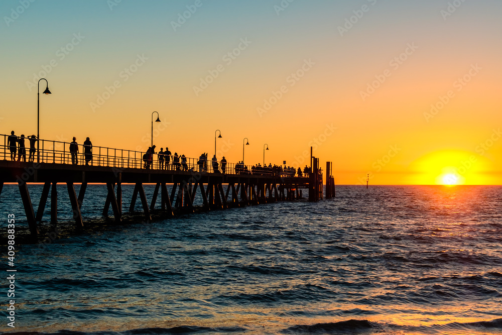 Glenelg Beach jetty with people walking along at sunset during summer evening