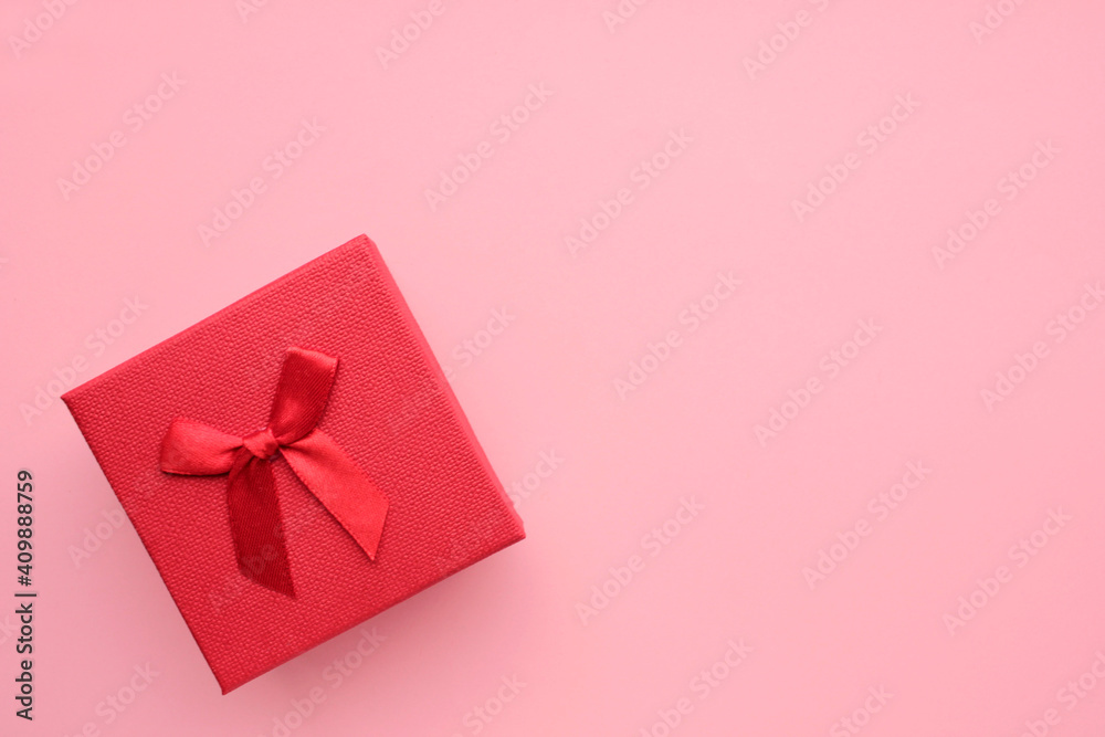 Red gift box with a bow on colored pink backdrop. Overhead view. Copy space. Valentines day or mothers day present