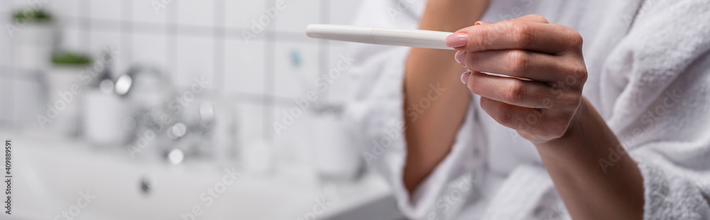 partial view of woman holding pregnancy test in bathroom