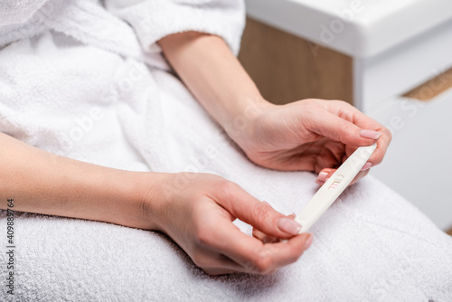 cropped view of woman in white bathrobe holding pregnancy test in bathroom