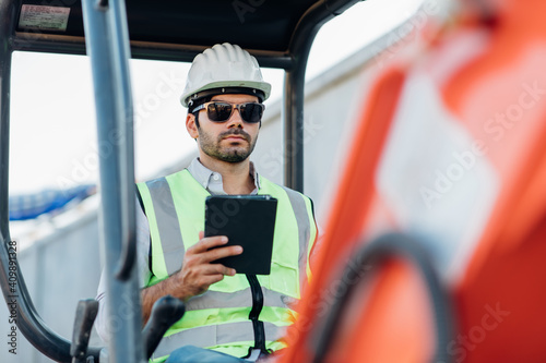 Construction Worker driving Excavator or Backhoe on construction building site. Young Hispanic Man operating heavy equipment