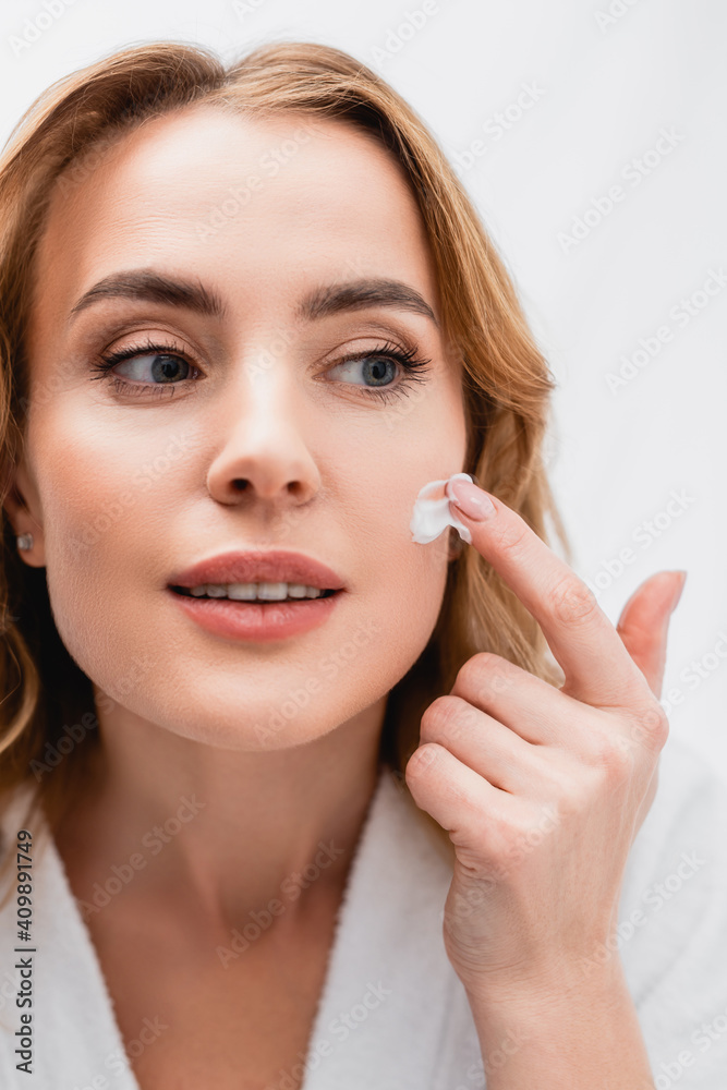 woman applying cosmetic cream on face in bathroom