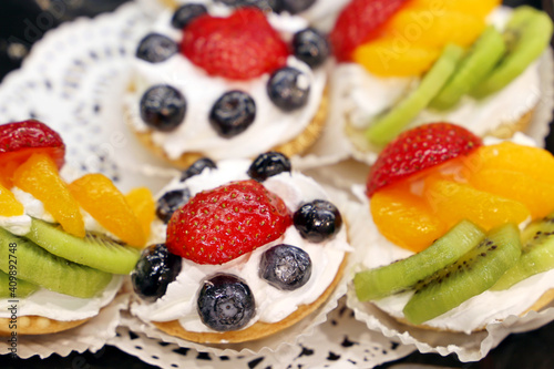 Creamy cakes with fresh fruits and berries. Sweet cream dessert with tangerines, kiwi, strawberry and blueberries