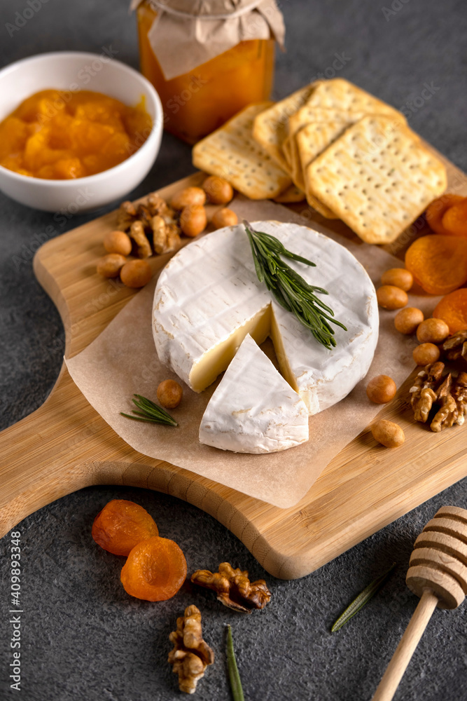 Brie cheese with nuts, pear slices and dried apricots. Camembert cheese. Brie cheese or Camembert cheese  on a wooden board. Tasty cheese starter.