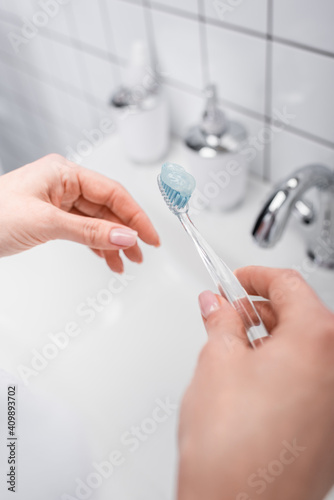 cropped view of woman holding toothbrush with toothpaste near sink
