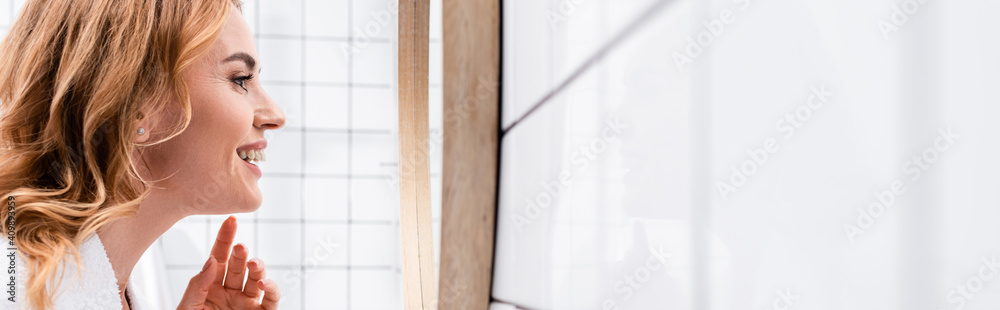 side view of happy woman looking at mirror in bathroom, banner