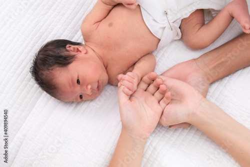 Beautiful shape hand of father, mother, daughter or sister hold tiny newborn hand on white bed with love, care and protection, infant look to mother face. baby hold his sister finger