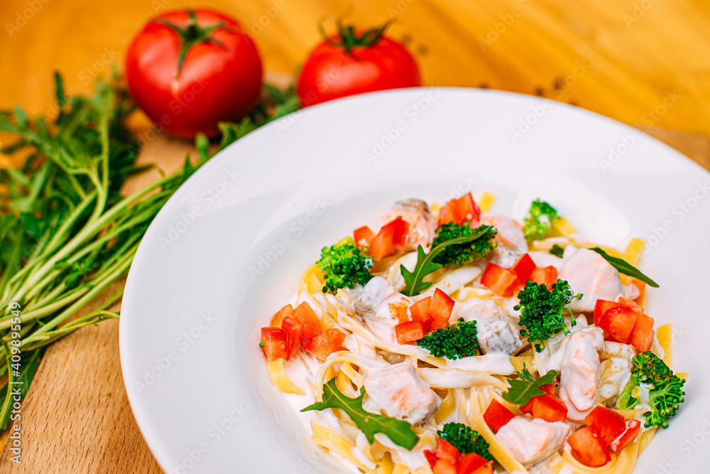 spaghetti with salmon, broccoli and tomatoes in a creamy sauce on a decorated table spaghetti with salmon, broccoli and tomatoes in a creamy sauce on a decorated table