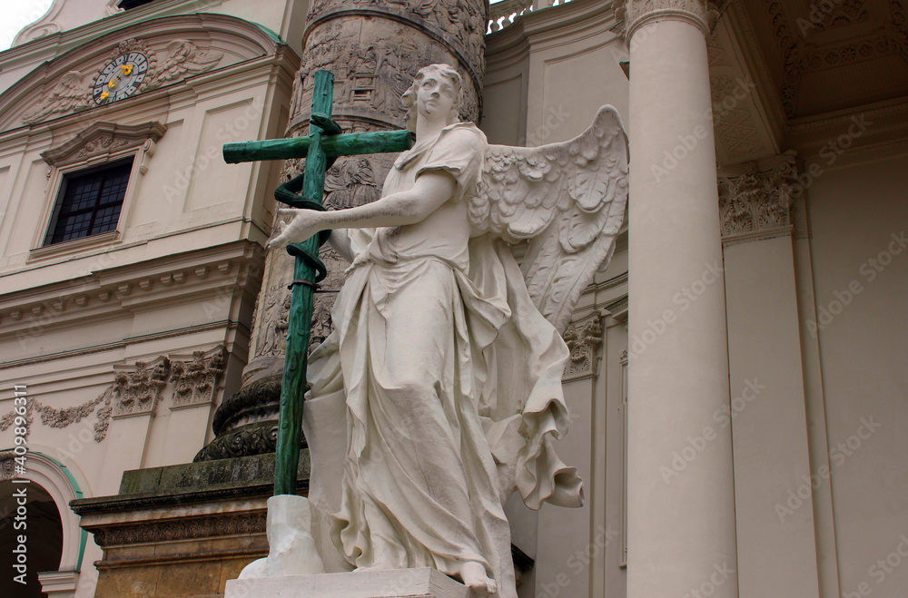 Angel statue with cross in front of Karlskirche (St. Charles's Church). An angel with wings holds a cross with a snake in his hands. The sculpture is located near the old church in Vienna.
