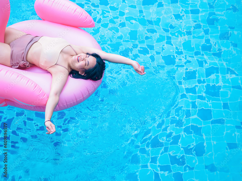 Chubby happy young woman dressed in swimsuit with inflatable flamingo in blue swimming pool.