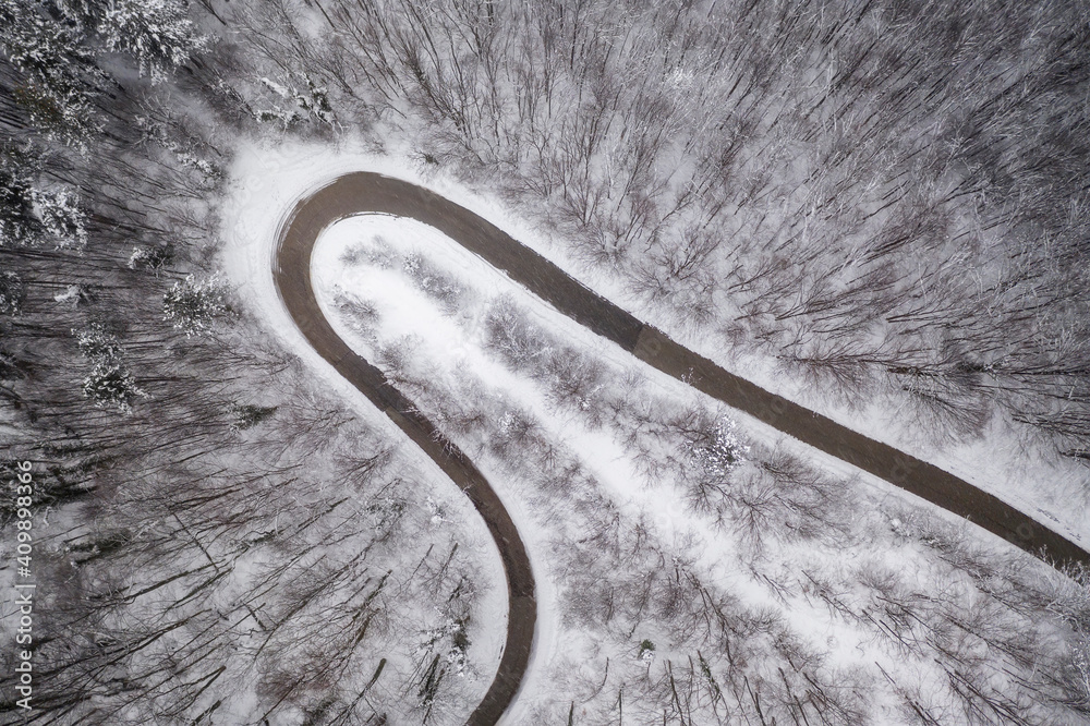 Top view with curvy mountain road in snow covered forest