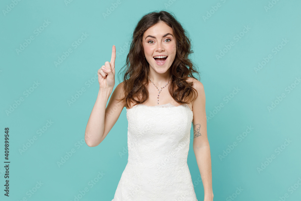 Excited tender bride young woman in beautiful white wedding dress holding index finger up with great new idea isolated on blue turquoise background studio portrait. Ceremony celebration party concept. Excited tender bride young woman in beautiful white wedding dress holding index finger up with great new idea isolated on blue turquoise background studio portrait. Ceremony celebration party concept.