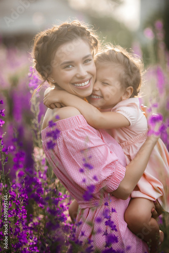 Young beautiful mother and her little daughter outdoors with flowers. Violet field of flowers and people there