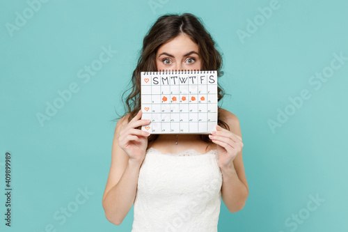 Konstfotografi Shocked bride young woman 20s in white wedding dress cover face with female periods calendar for checking menstruation days isolated on blue turquoise background