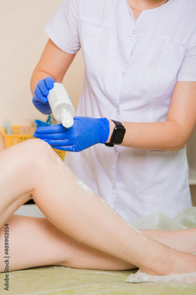 Hands in gloves of a woman depilation specialist in the process of working in a beauty salon. A girl in a white coat, a beauty salon worker rubs her legs with an antiseptic, preparing for hair removal Hands in gloves of a woman depilation specialist in the process of working in a beauty salon. A girl in a white coat, a beauty salon worker rubs her legs with an antiseptic, preparing for hair removal