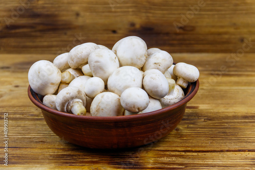 Fresh champignon mushrooms in ceramic bowl on the wooden table