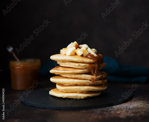 American pancakes with caramel and banana on a dark background