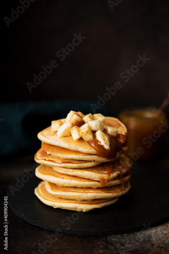 American pancakes with caramel and banana on a dark background, selective focus