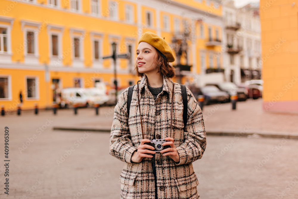 Pretty girl in bright beret looks at urban architecture with enthusiasm. Lady in stylish autumn coat holding retro camera Pretty girl in bright beret looks at urban architecture with enthusiasm. Lady in stylish autumn coat holding retro camera
