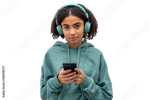 Black teenager looking at camera while using smartphone and listening to music isolated on white background