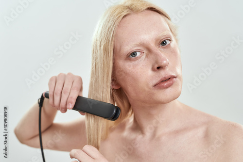 Portrait of young man using tool for straightening hair